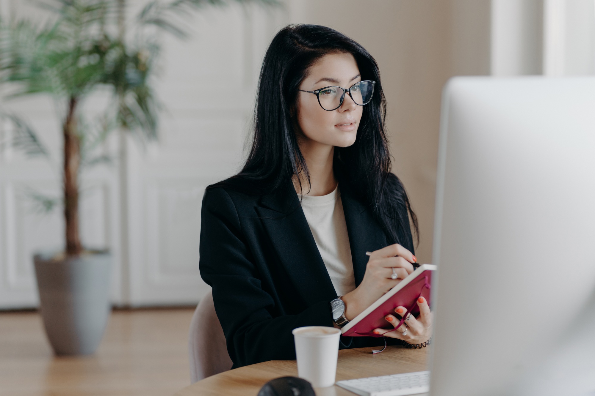 Businesswoman makes notes in notepad, concentrated in computer screen, watches training video